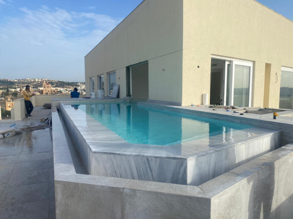 Outdoor rooftop swimming pool under construction on top of a building with a city view in the background.