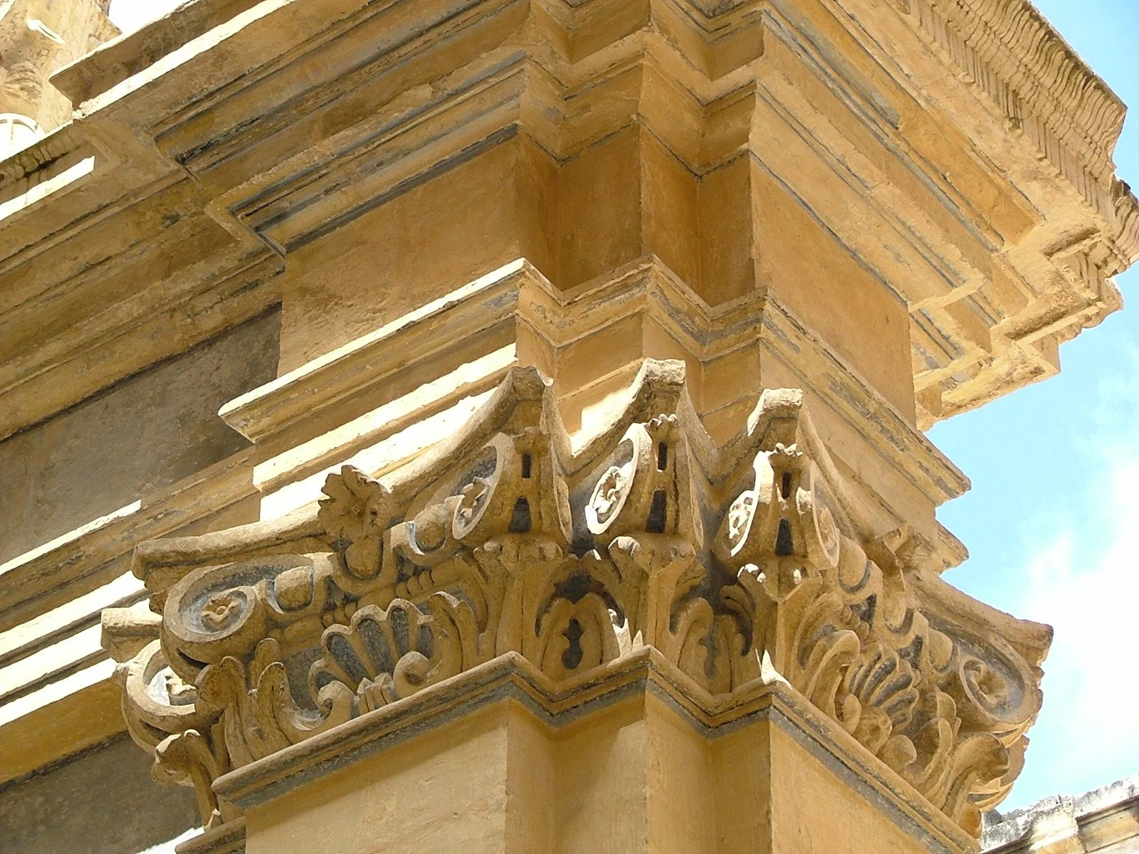 Close-up of an ornate, carved stone architectural detail on a building corner, with decorative scrolls and floral motifs.