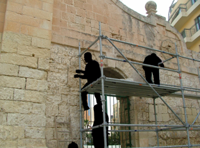 Silhouettes of two workers on scaffolding repairing or working on the stone wall of a historic building.