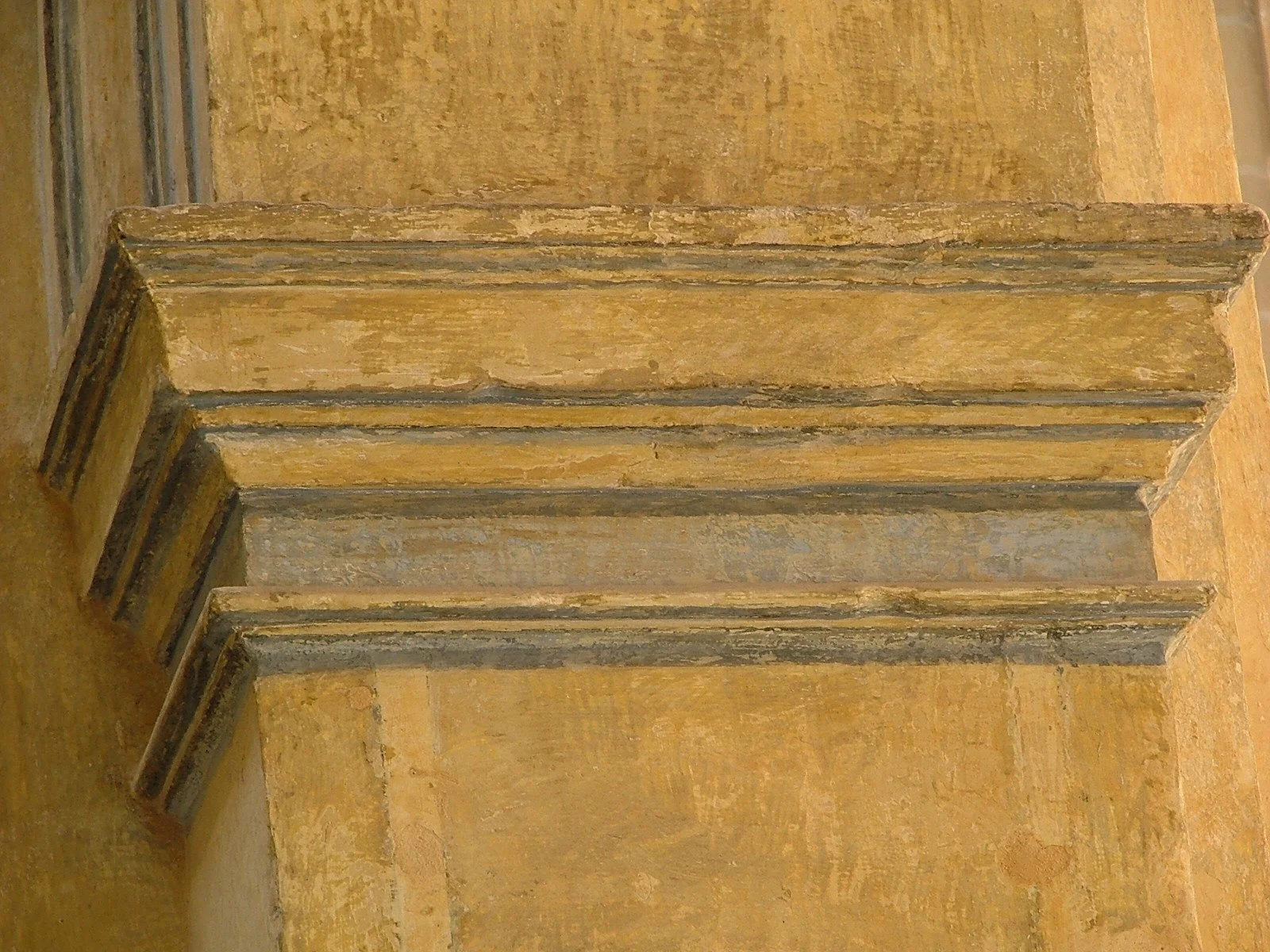 Close-up of a worn, yellowish stone staircase with dark gray trim at the edges, attached to a matching yellowish stone wall.