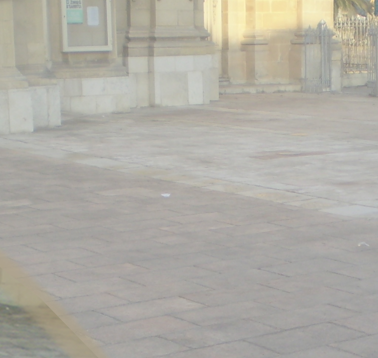 Empty paved sidewalk with a building and gate in the background.