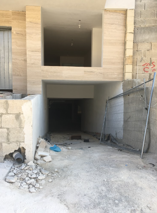 Building under construction with unfinished entrance and exposed concrete, debris on ground, and construction fencing.