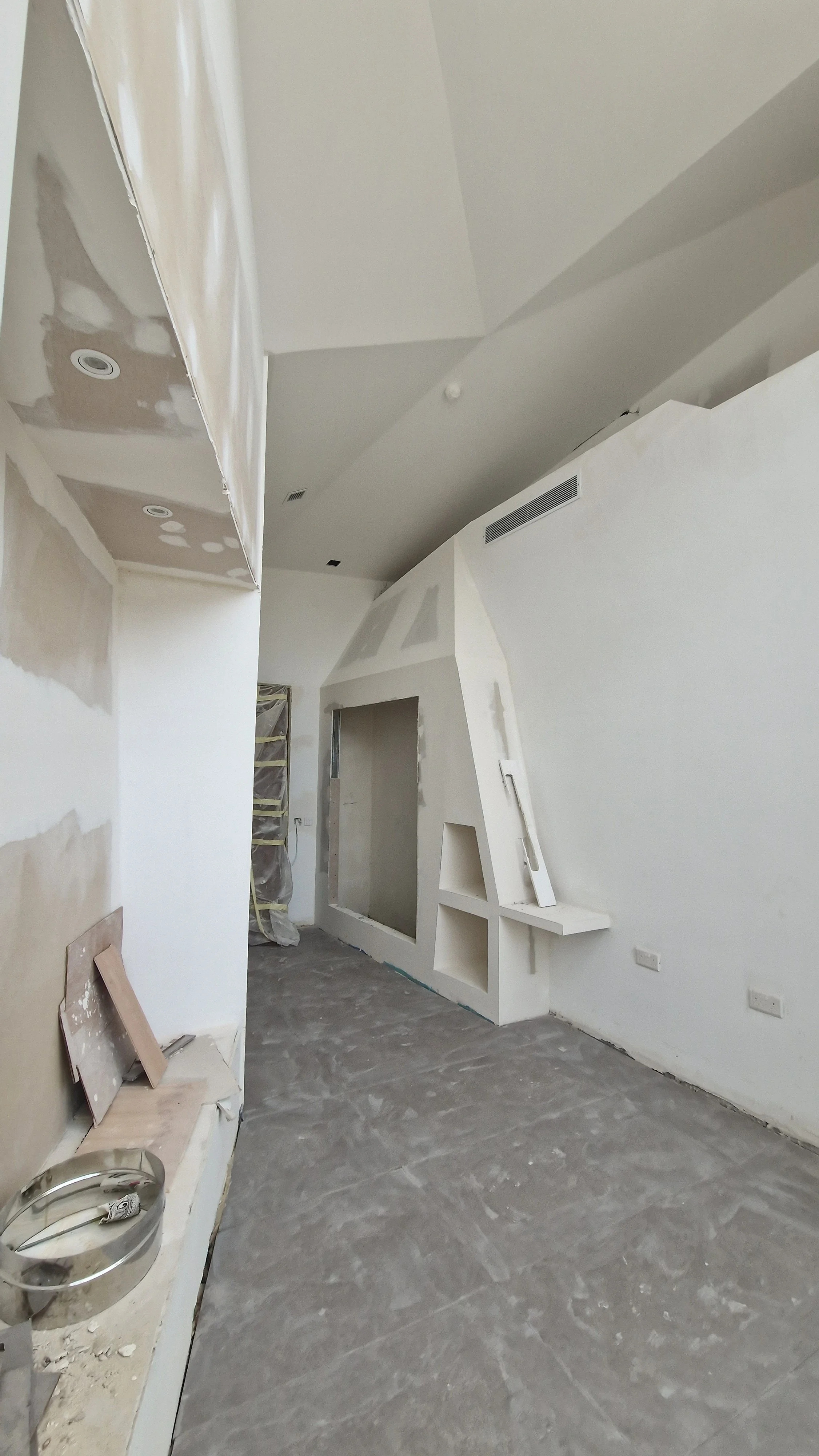 Room under construction with unfinished walls, ceiling, and flooring. Wall has a fireplace opening, with some drywall and construction materials present.