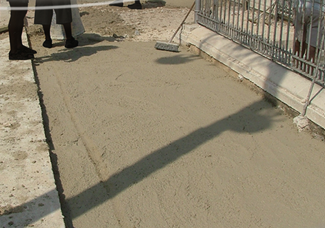 A construction site with freshly poured concrete and a few people standing nearby.