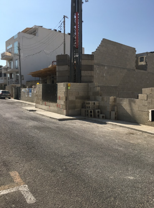 Construction site with a partially built brick wall and a construction lift on a city street.