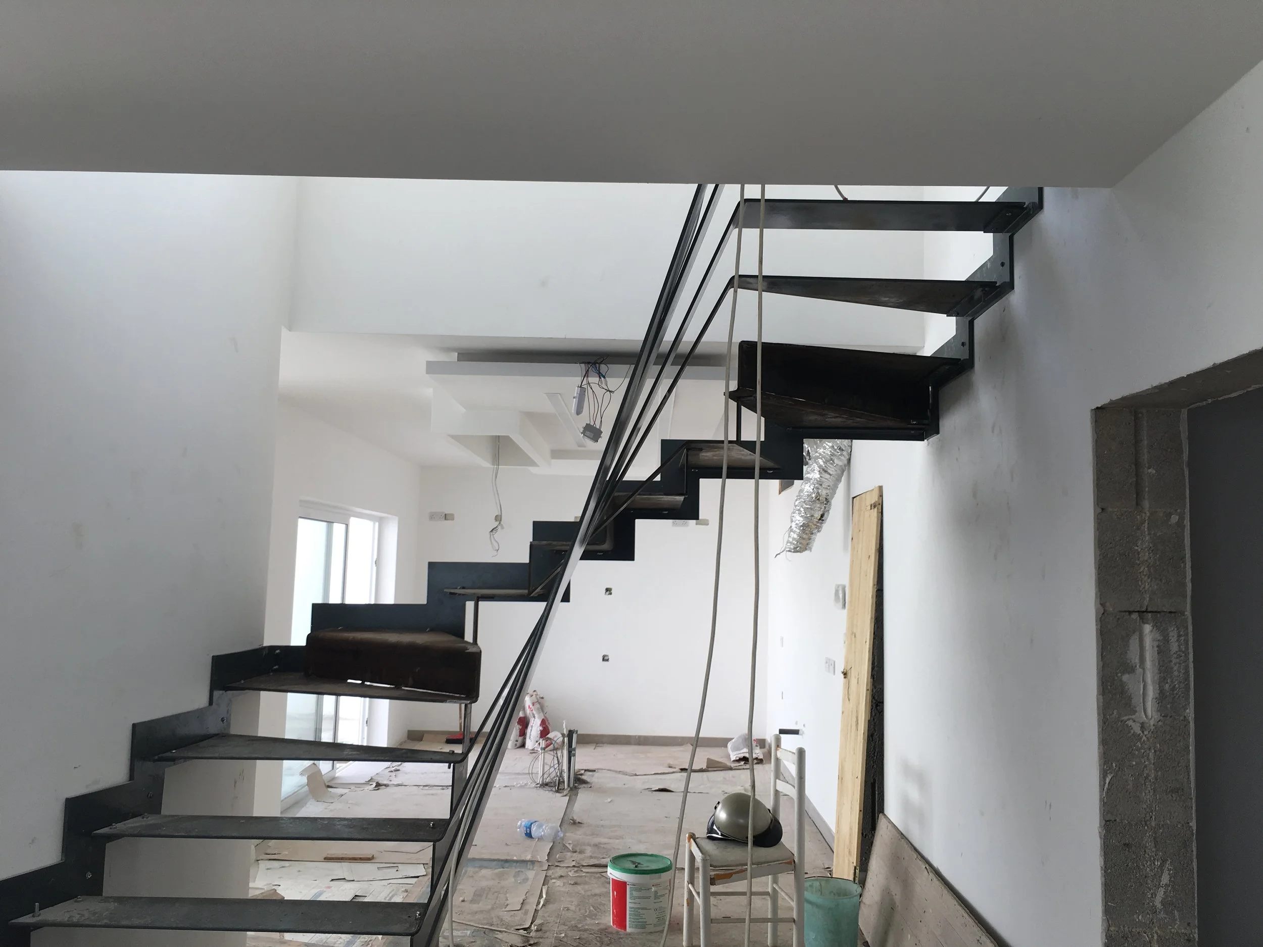 Interior of a house under construction with a black staircase, construction tools, and materials scattered around.