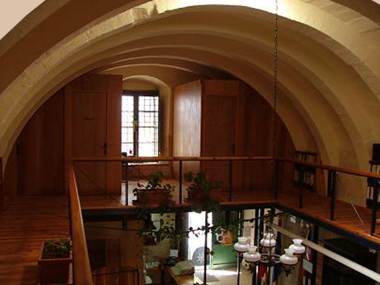Interior view of a space with arched ceilings, wooden floors, a wooden railing, and a curved window with multiple panes.