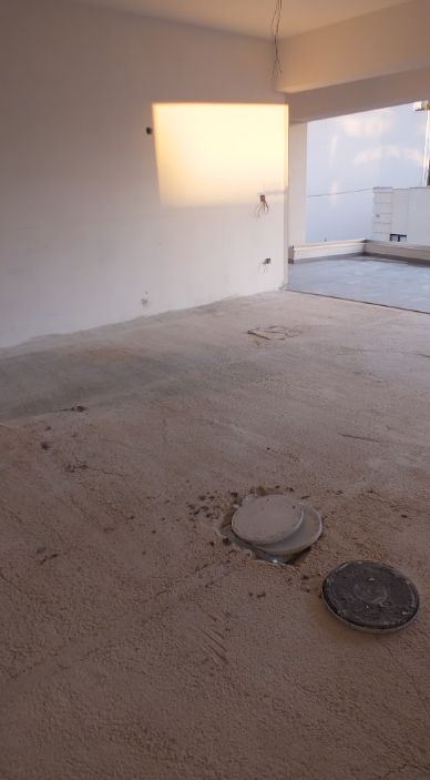 Empty room under construction with an unfinished floor, a recessed area in the wall, and a view of the city skyline through large windows.
