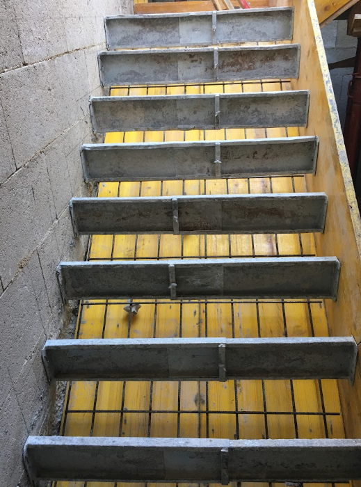 Construction staircase with yellow treads and metal supports, next to a concrete wall.