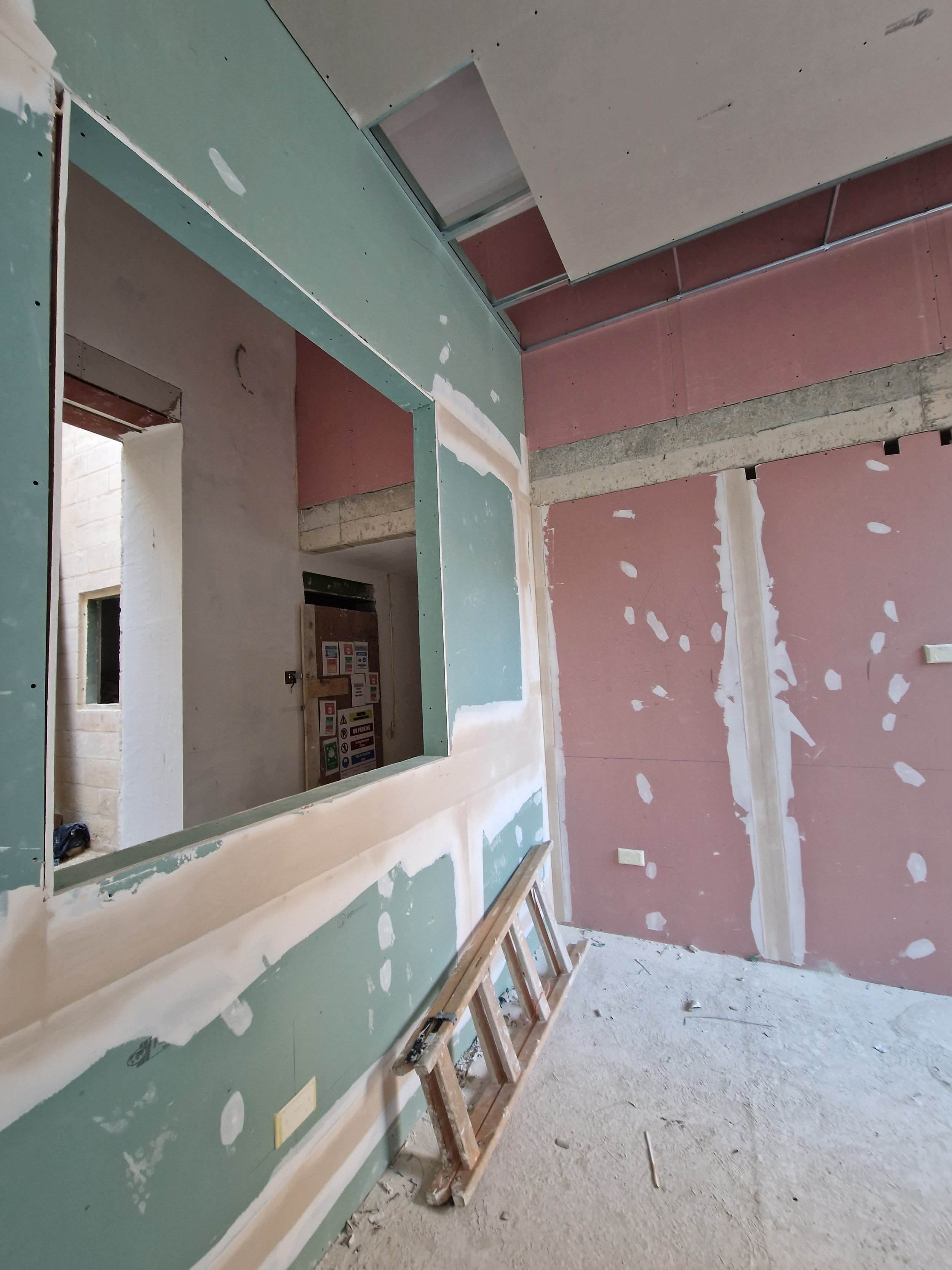 An interior view of a building under construction with unfinished walls, drywall and insulation visible, and a ladder leaning against a wall.