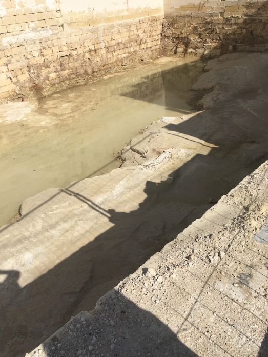 Construction site with a partially excavated area filled with water, surrounded by brick and concrete walls.