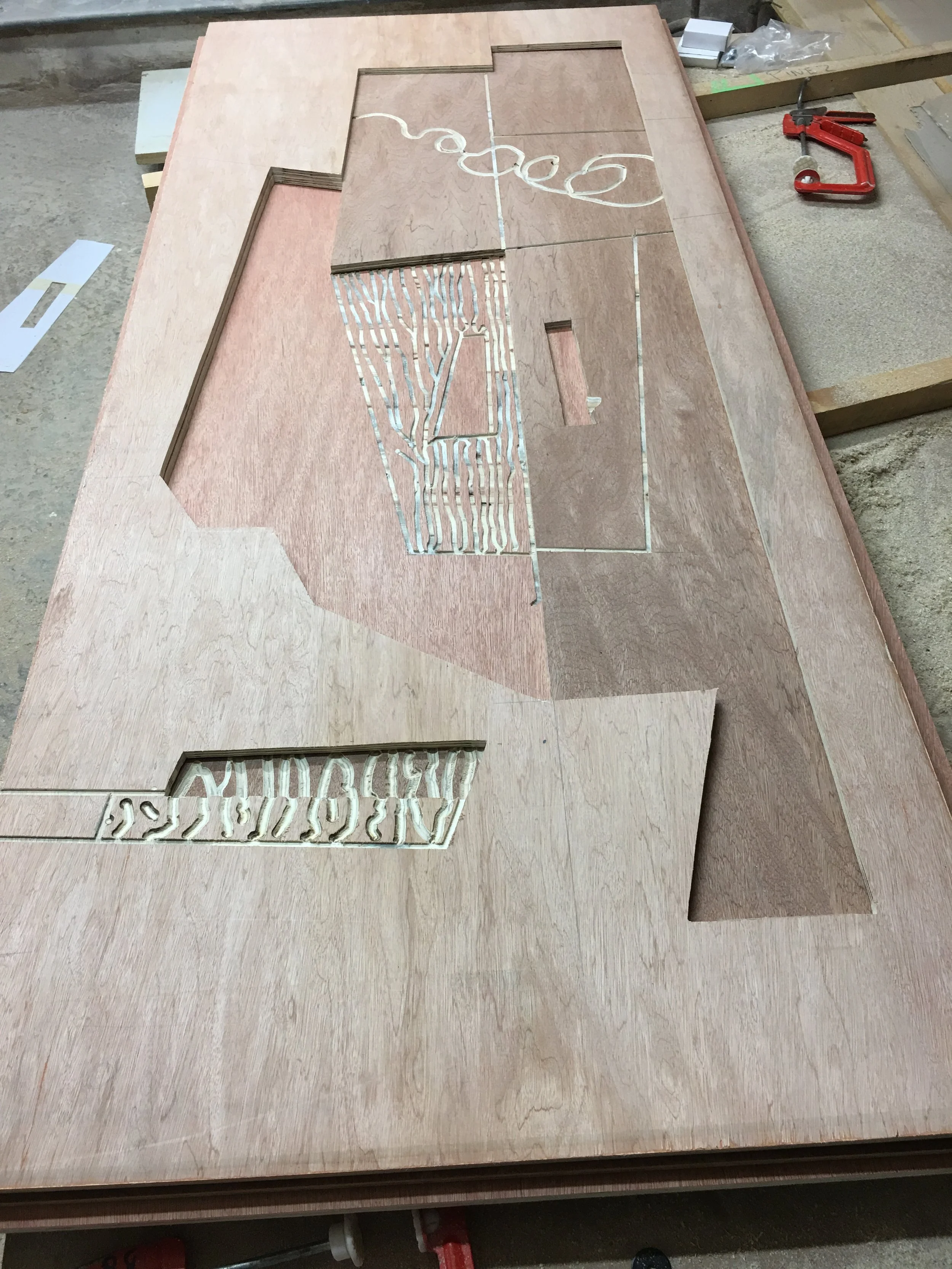 A woodworking project in progress featuring a wooden panel with cut-out designs. The panel is placed on a workbench with tools and materials nearby.