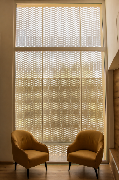 Two yellow armchairs facing each other in front of a large window with a dotted pattern, inside a room with wooden flooring and a wall on the right.