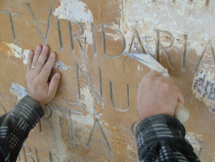 A person carving or restoring inscriptions on an old stone or monument with a tool in their hand.