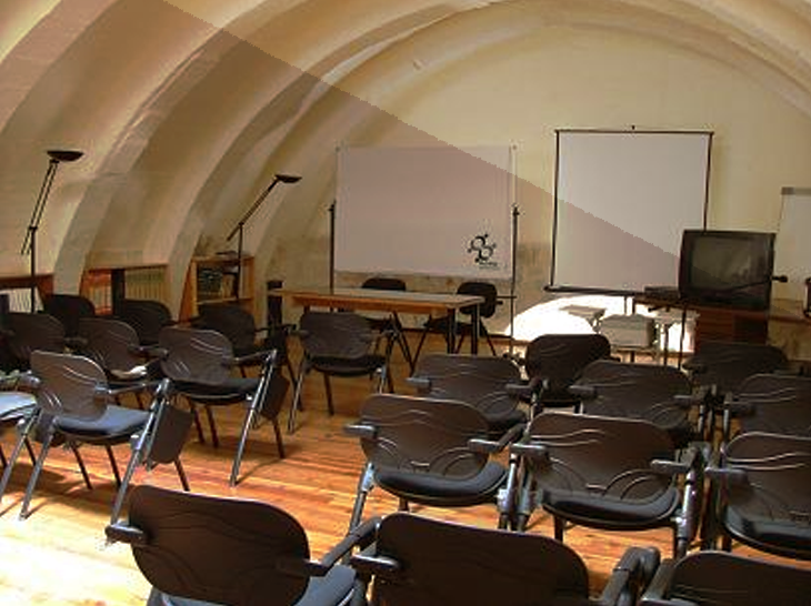 Empty classroom or training room with chairs facing a whiteboard and a projector screen, in an arched ceiling room with wooden flooring.