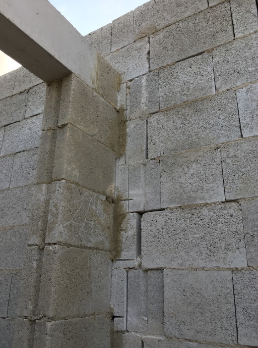 Corner of a cinder block wall under construction, with unfinished brickwork and a concrete beam extending from the wall.