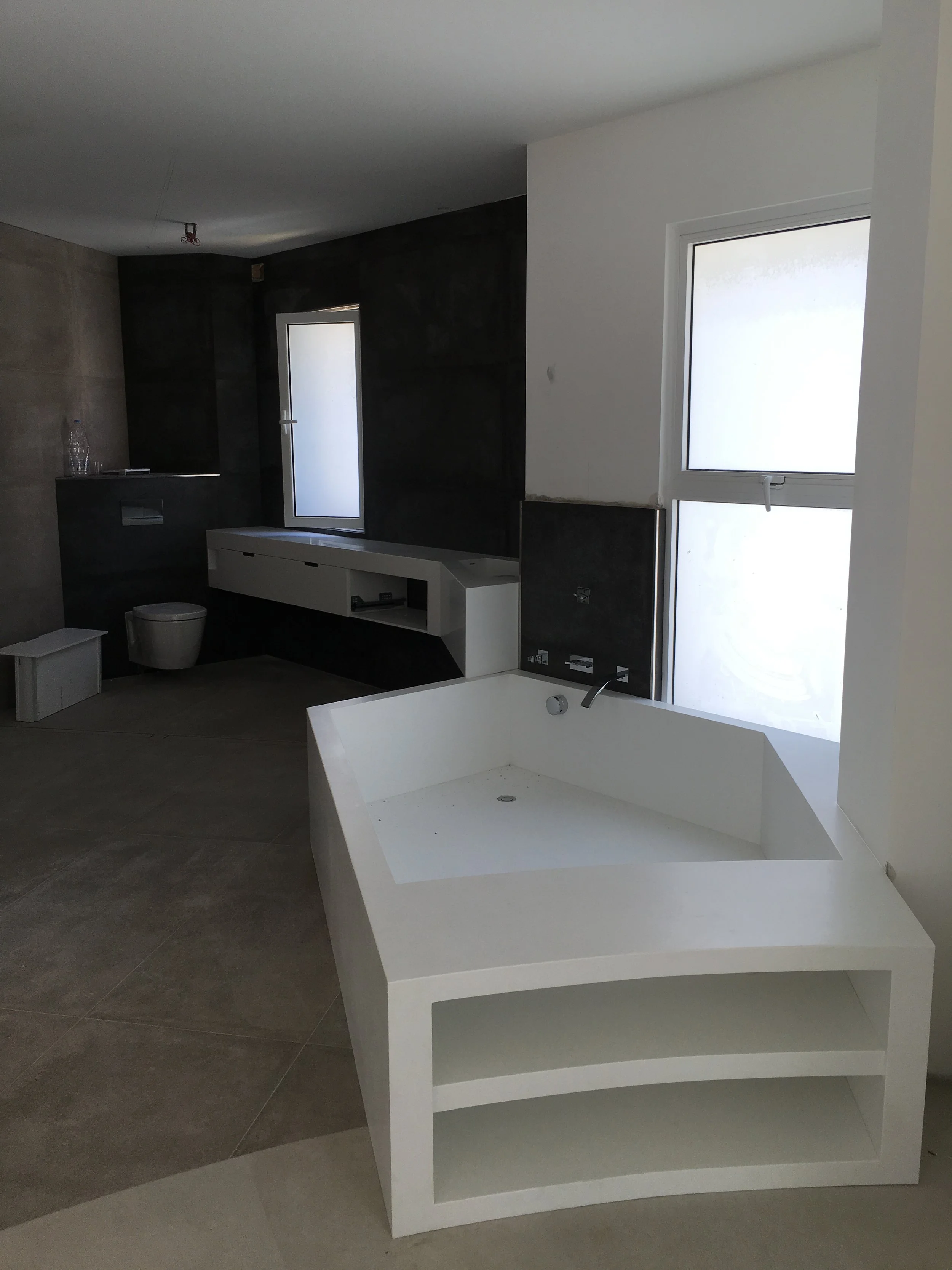 Interior of a house under construction with a large white bathtub, a window, and various unfinished fixtures.