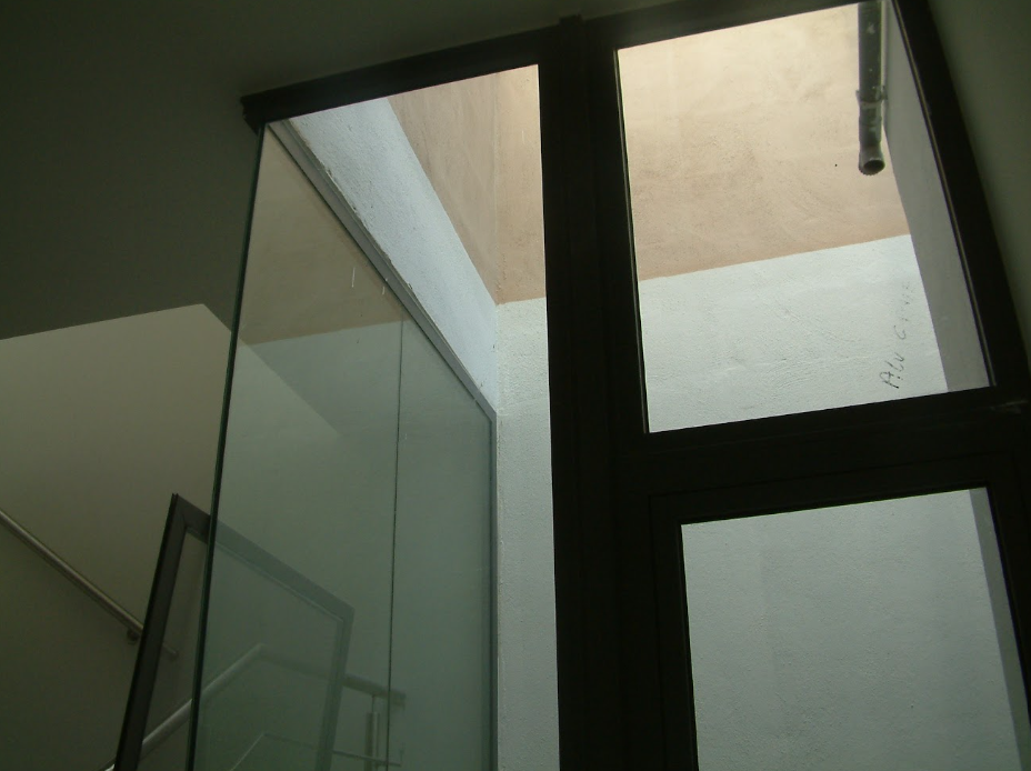 Close-up of a window with black frames, showing a view of the outside wall with textured surface and some writing on it.