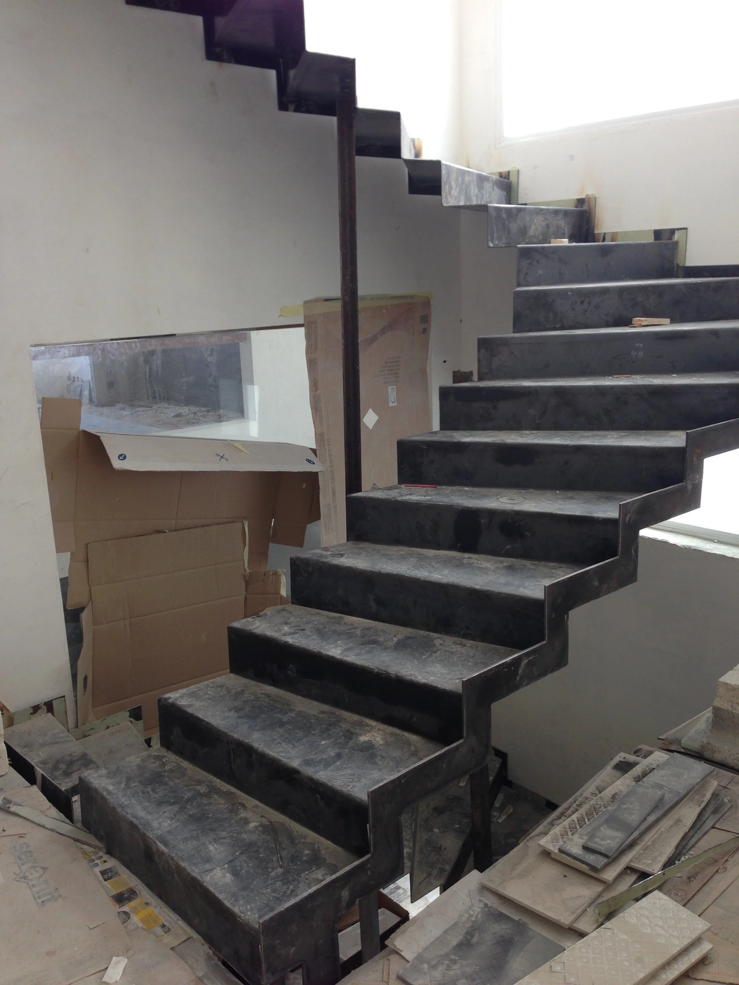 Inviting floating staircase with black marble steps and a simple metal handrail, under construction in a bright, minimally decorated interior with a large window