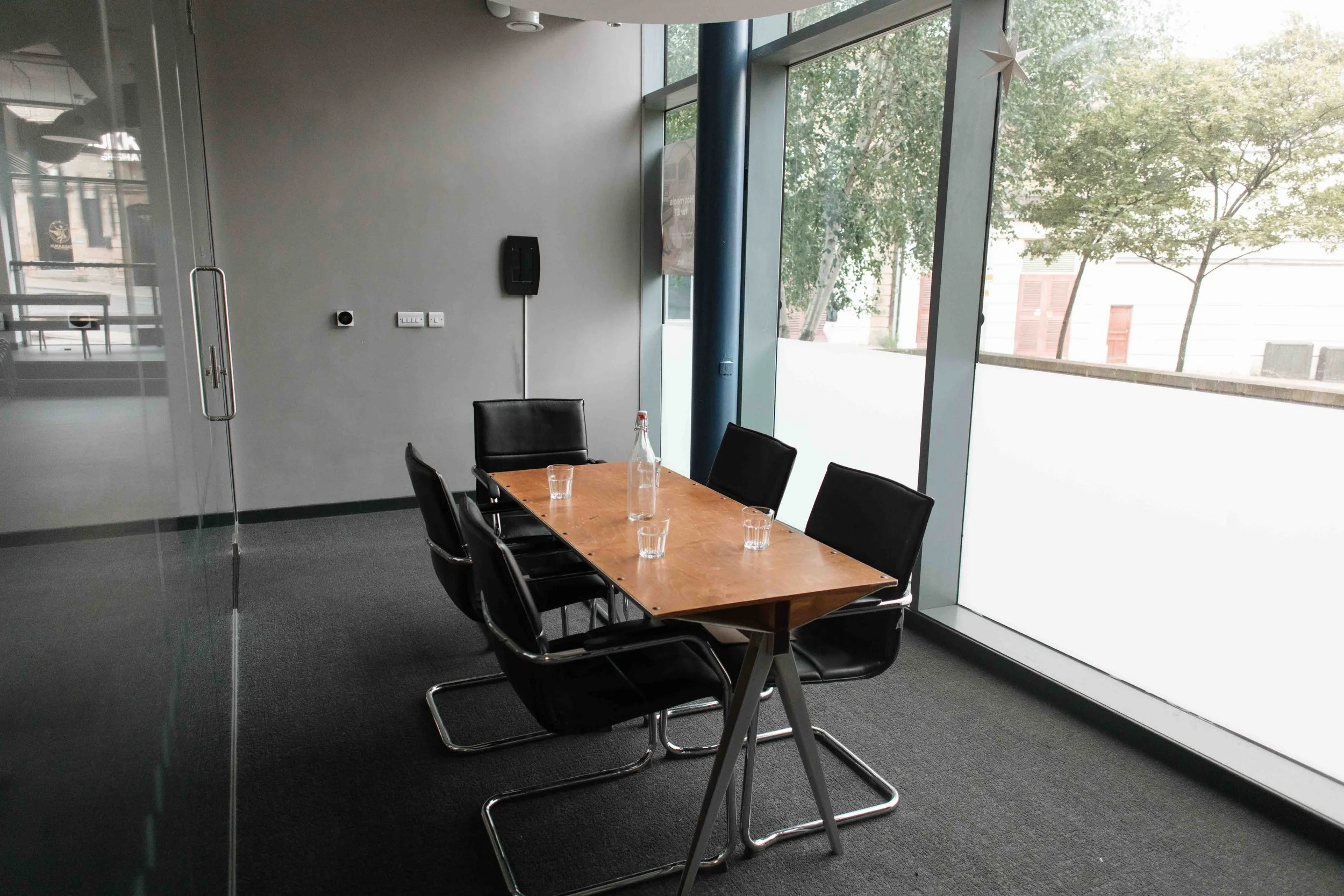Bradford meeting room with a rectangular wooden table, black chairs, large windows with trees outside, and minimal decor including a star-shaped hanging ornament.
