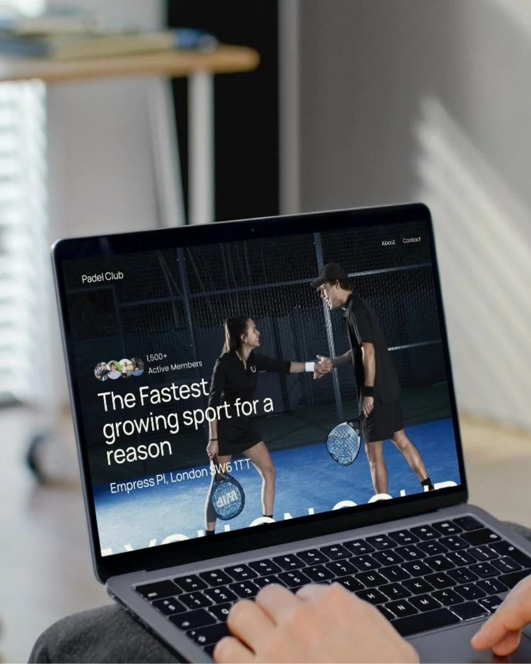 A person using a laptop showing a website about a padel court, with two people on a padel court shaking hands, holding rackets, and smiling.