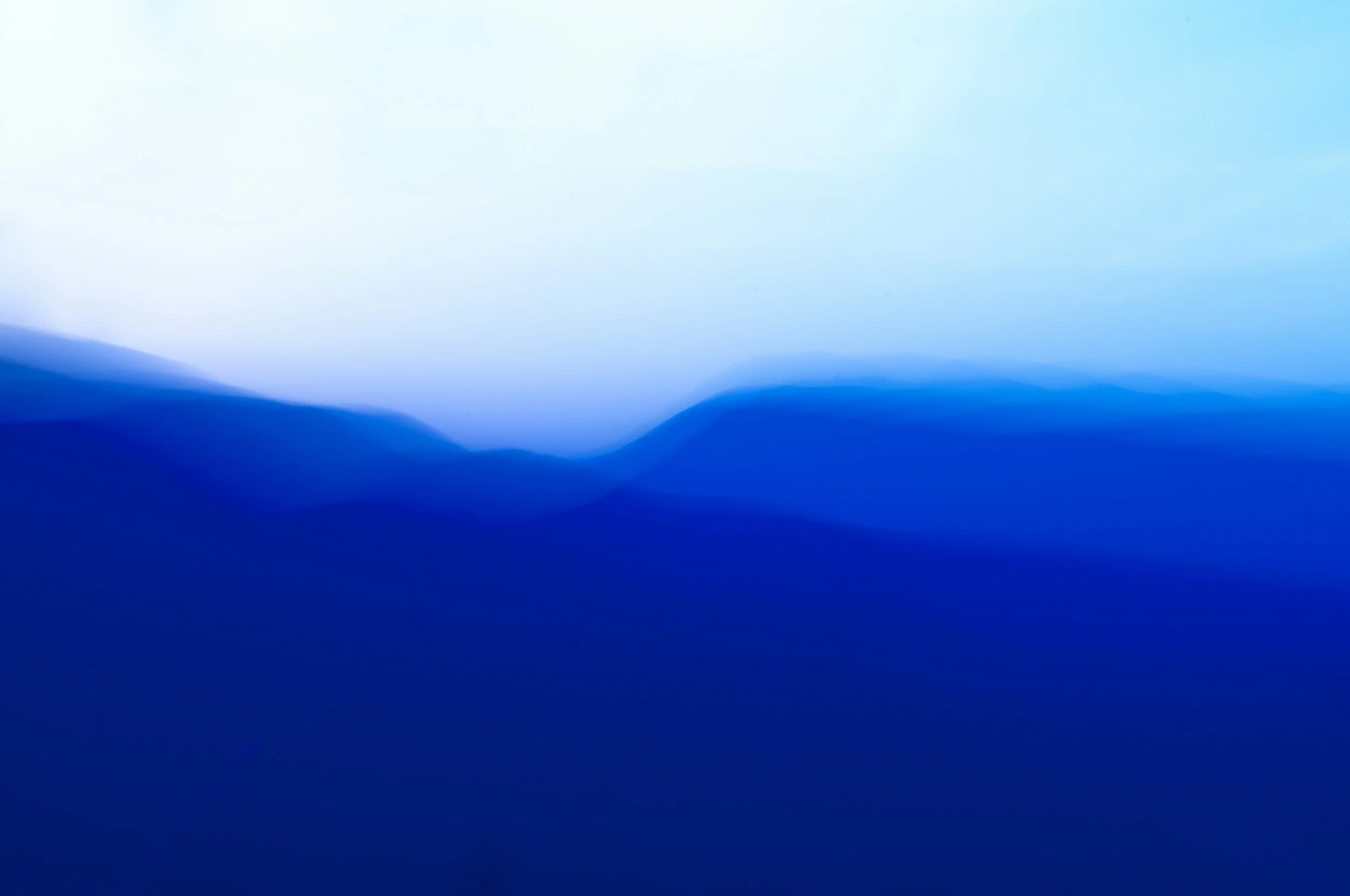 A landscape view of snow-capped mountains in the background, with rolling brown and green hills in the foreground, and a modern building nestled on the hillside.