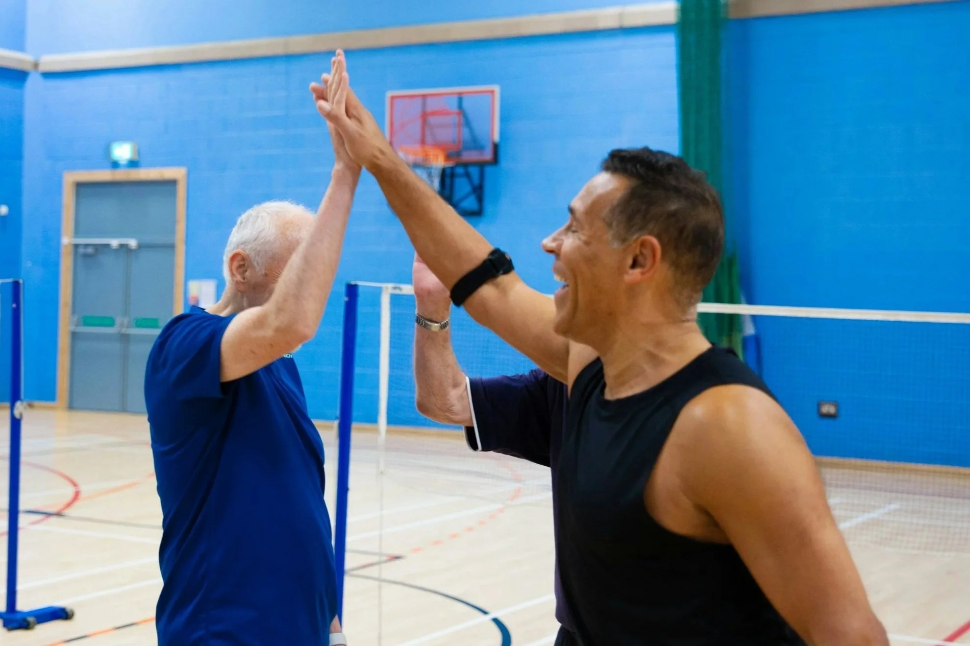Modern building with wood and white exterior, large glass window, set in mountainous landscape with grassy foreground.