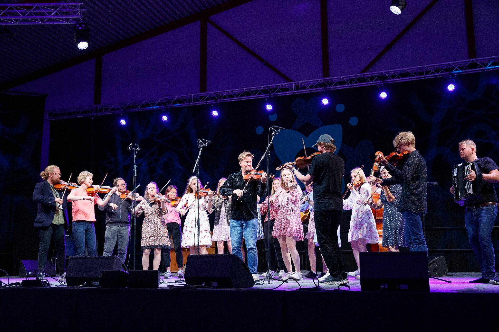 En gruppe med mennesker som spiller fiolin på en scene under en konsert, med lys og mikrofoner.