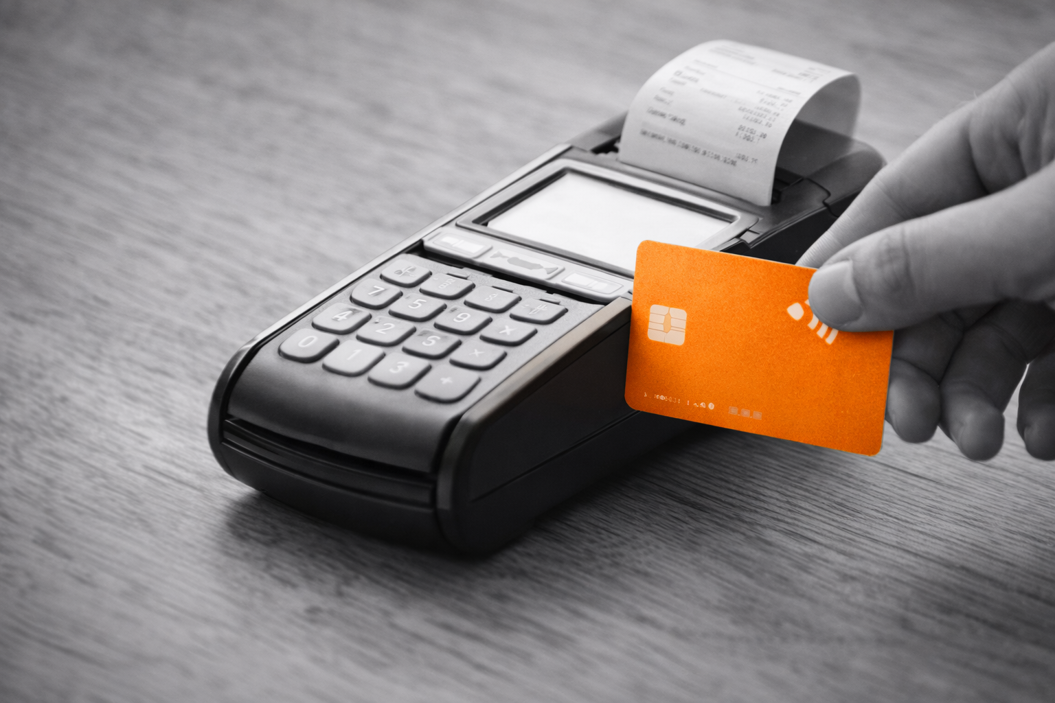 A hand inserting an orange contactless credit card into a point-of-sale terminal with a printed receipt coming out.