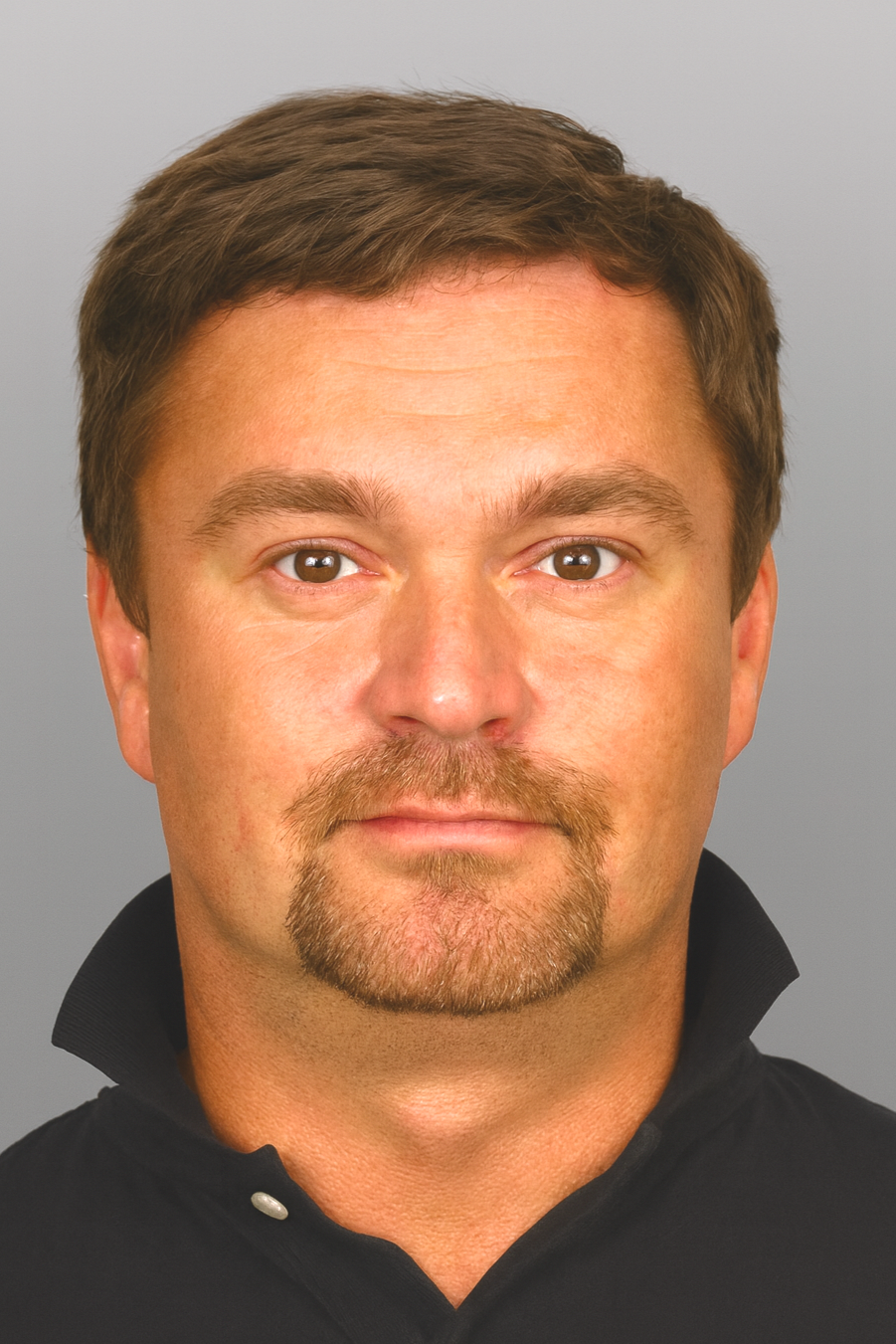 Photo of a man with short dark hair, facial hair, wearing a collared shirt with the collar up, looking directly at the camera.