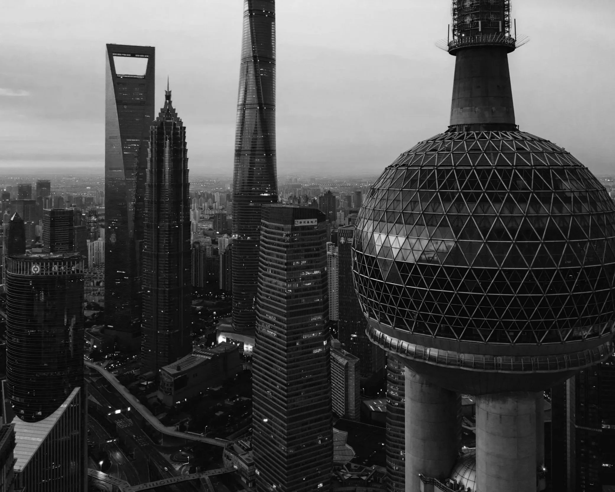 Black and white photograph of a city skyline with tall skyscrapers, including the distinct spherical TV tower of Shanghai, China.