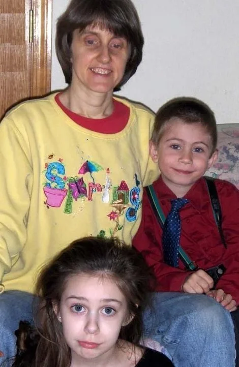 Charlene Clough smiling, sitting with  a girl with long brown hair in front,  all indoors.
