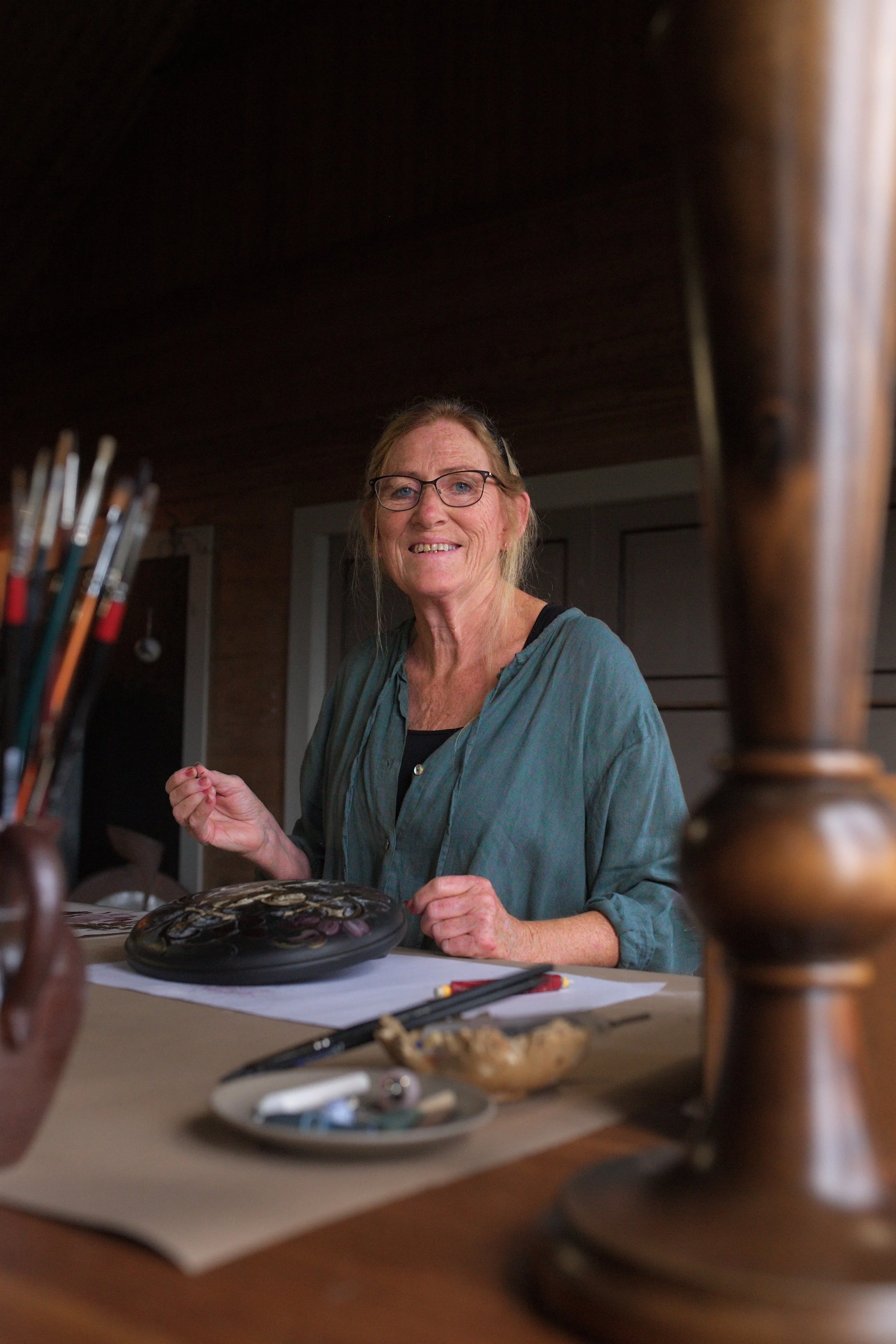 Anne Hesvik som sit og malar i atelieret sitt, omgitt av kunstutstyr.