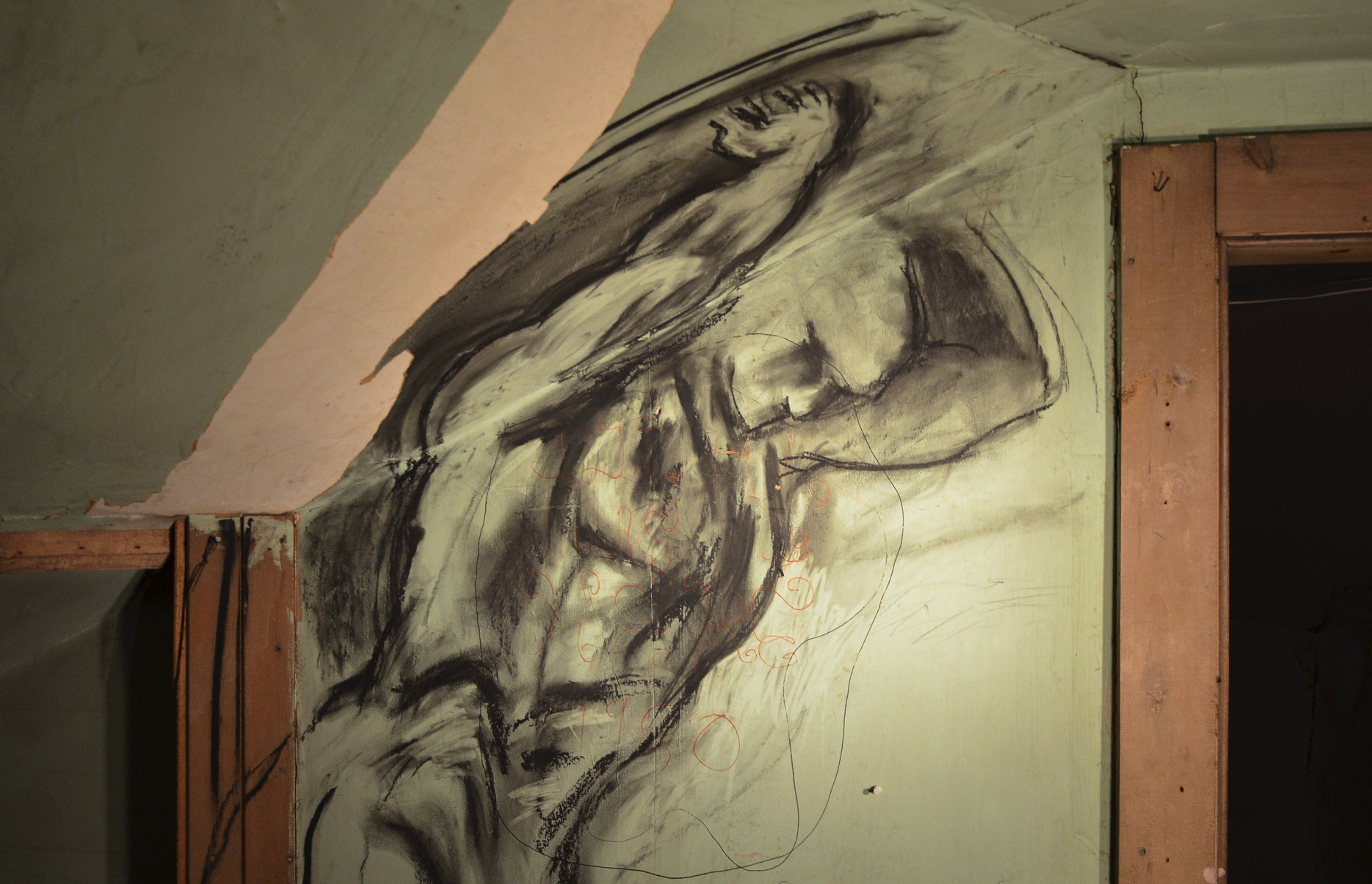 Charcoal drawing of a muscular human figure on a wall in an interior space.