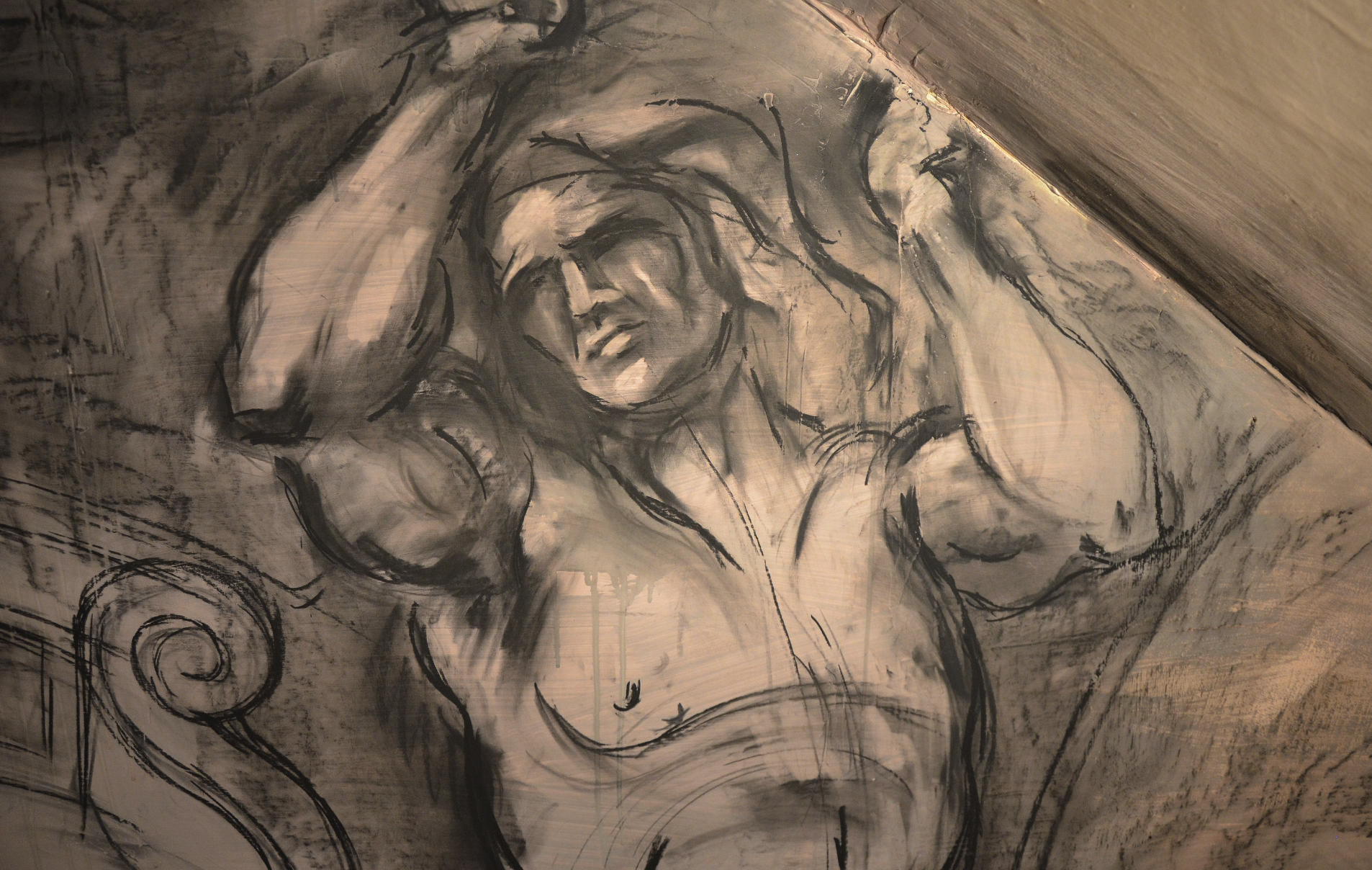 Charcoal drawing of a muscular figure with raised arms on a textured surface, featuring dynamic lines and shadowing.