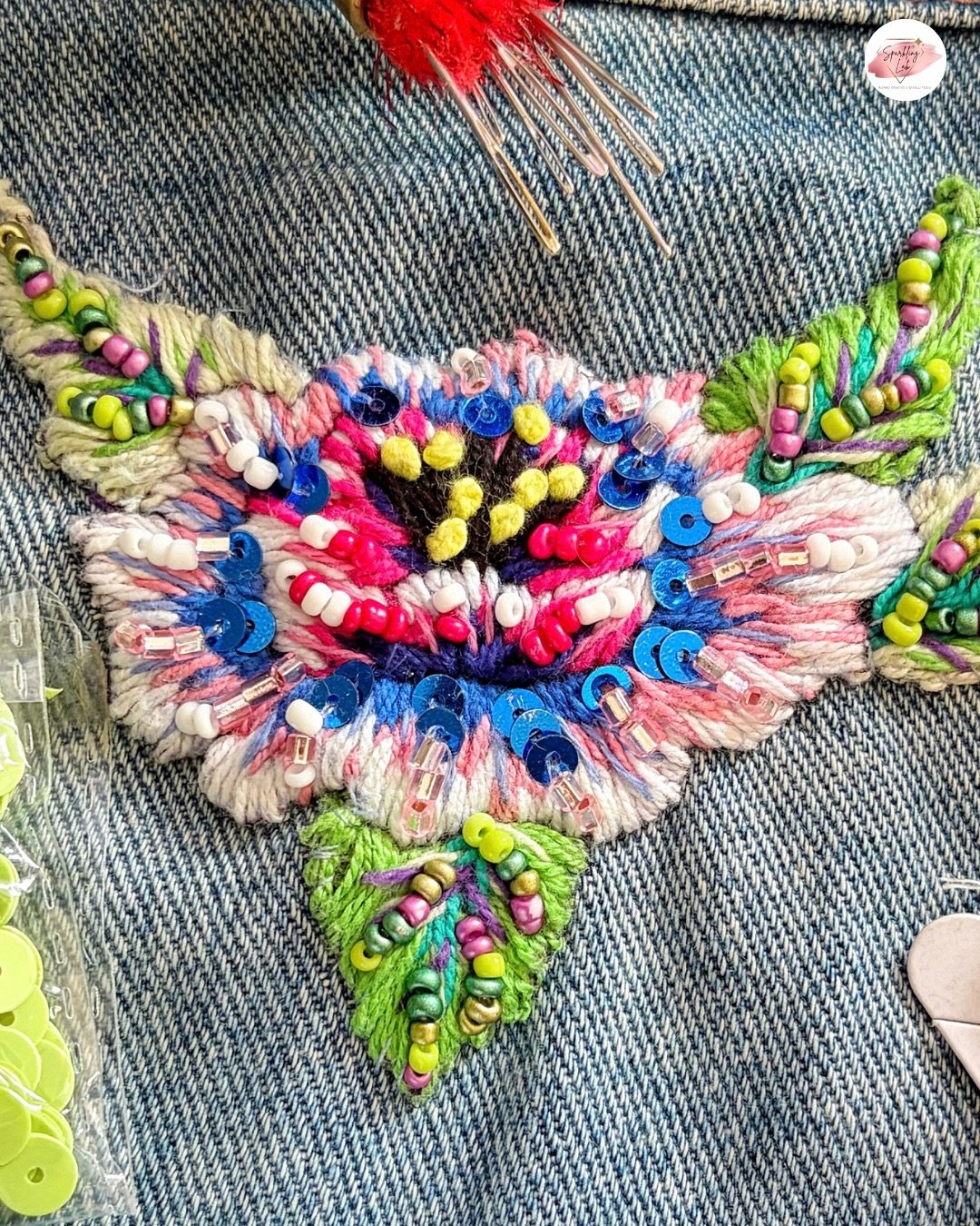 dettaglio macro di punti di ricamo su denim con perline e fili colorati, tecnica di personalizzazione dei capi