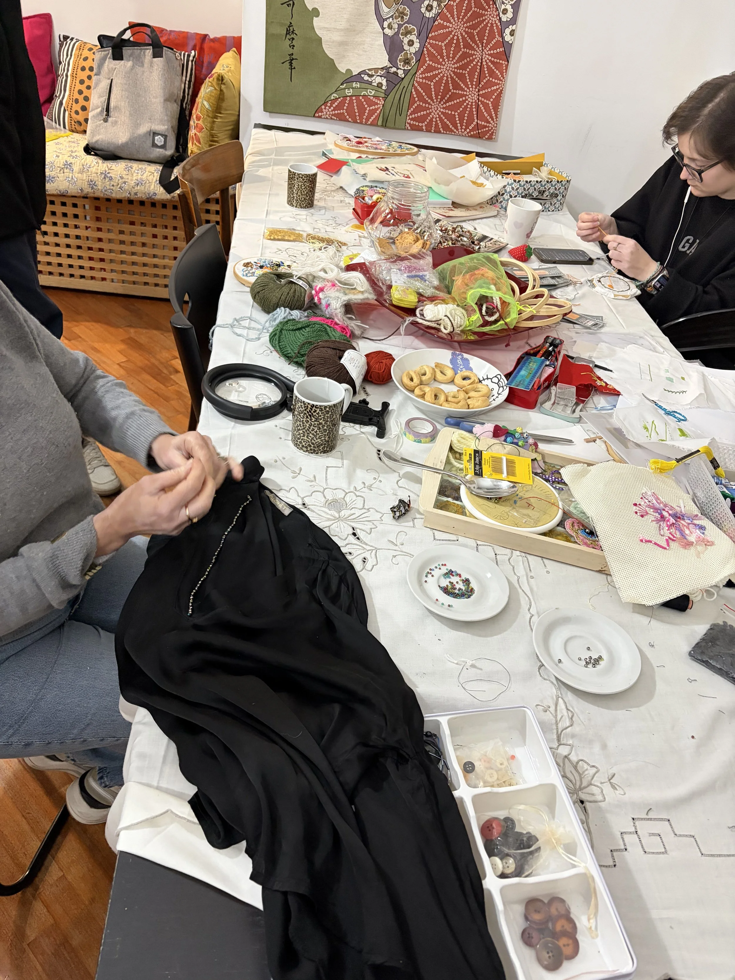 Partecipanti al Club del Ricamo lavorano su capi personali con ago e filo, perline, paillettes e strass, riparando e decorando vestiti.