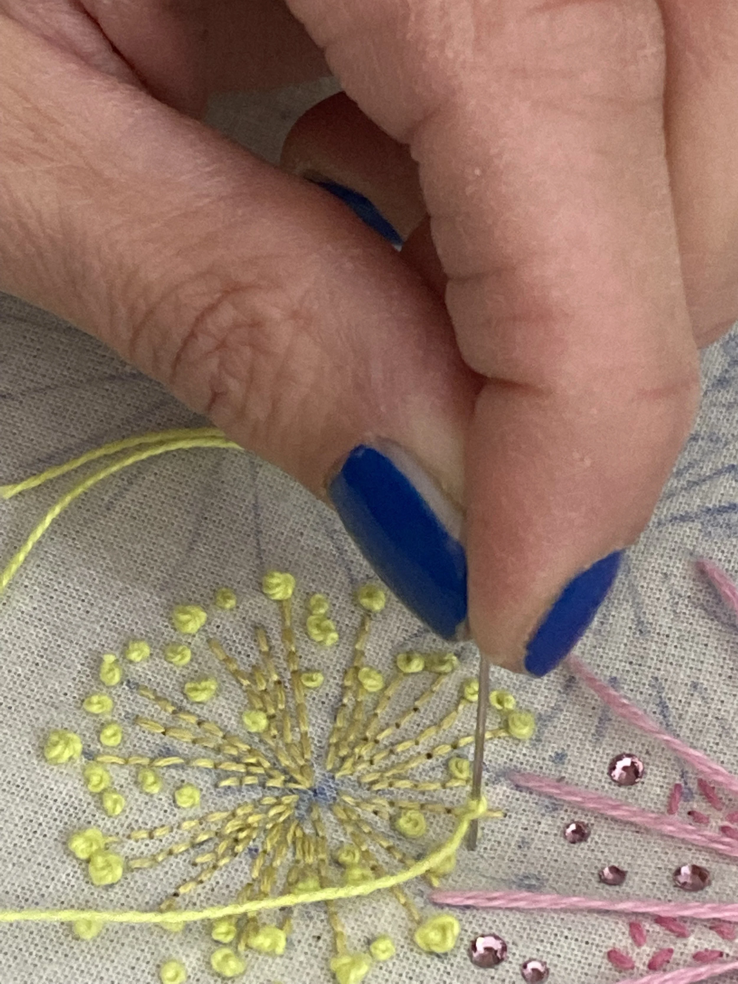 Ricamo a mano con filo colorato e perline su tessuto, con una mano che tiene l'ago.