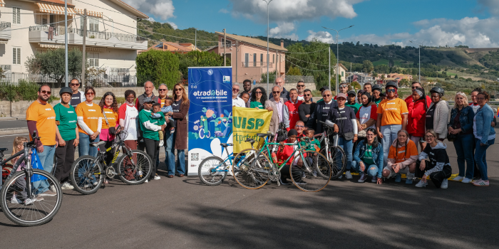Gruppo di persone con biciclette in una competizione o evento, con banner e strutture di sostegno sullo sfondo.