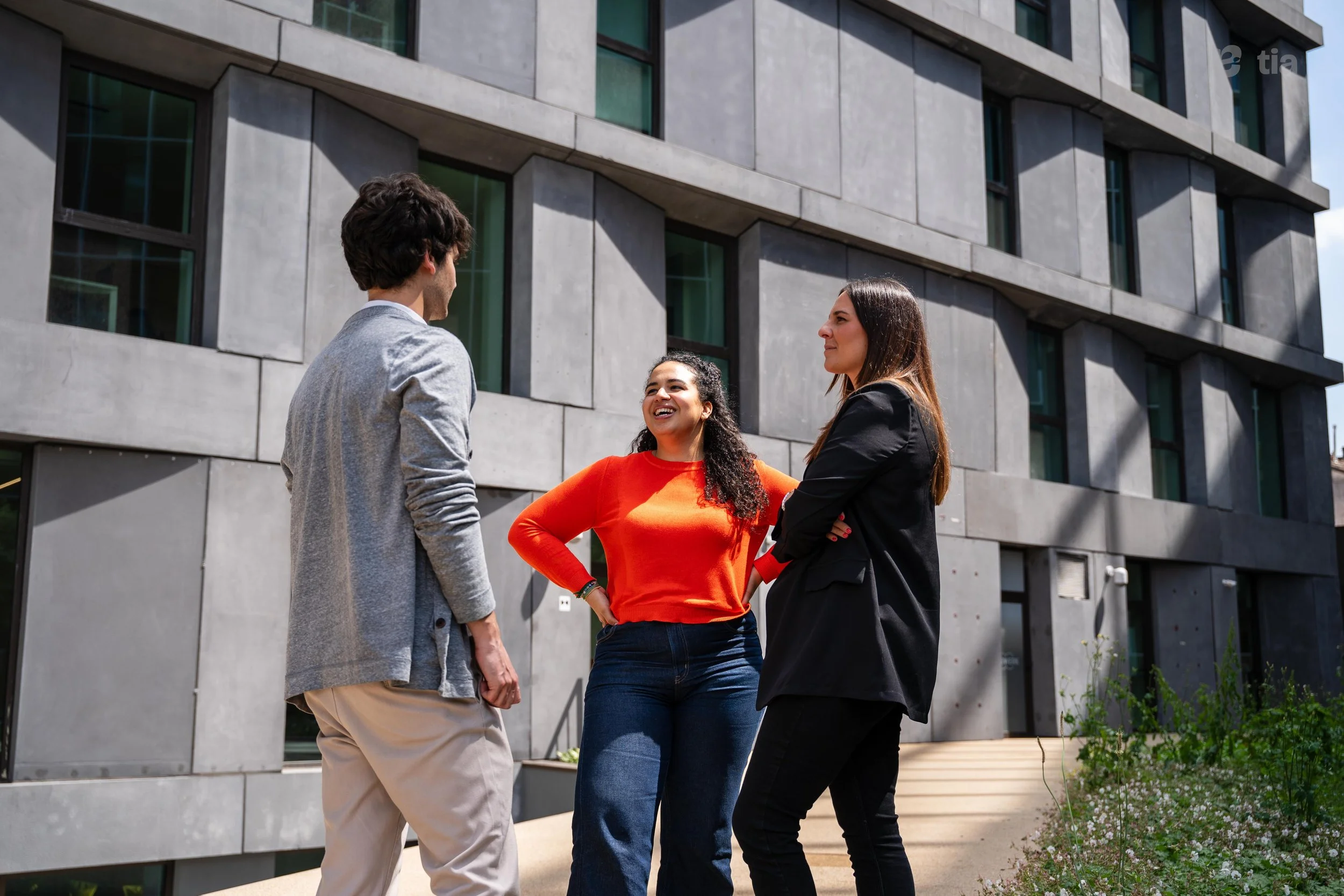 Tre persone si incontrano e conversano all'aperto davanti a un edificio moderno con finestre a specchio.