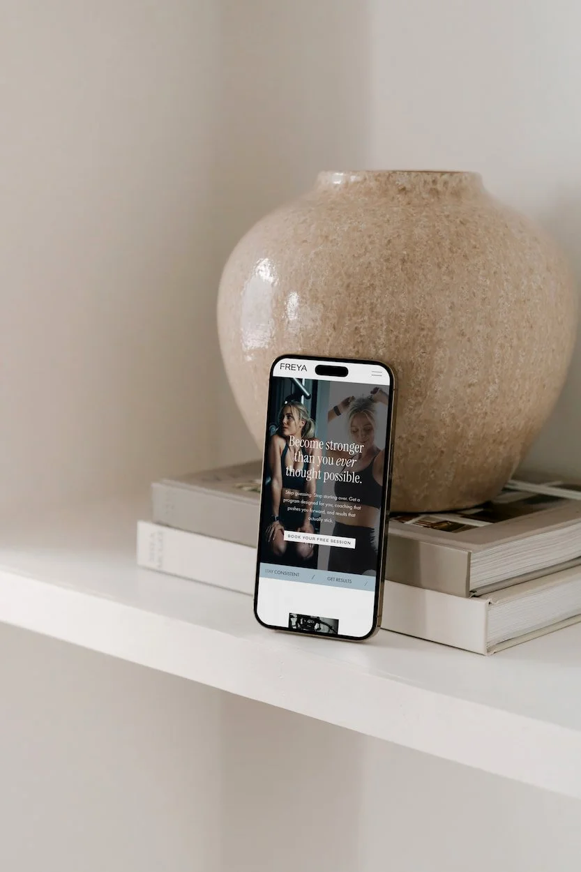 mock up of an iphone showing a fitness website leaning against a marble vase placed on two coffee table books