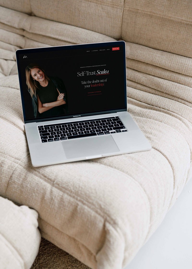 mock up of a website with a black web page, on a laptop rested on a beige styling sofa