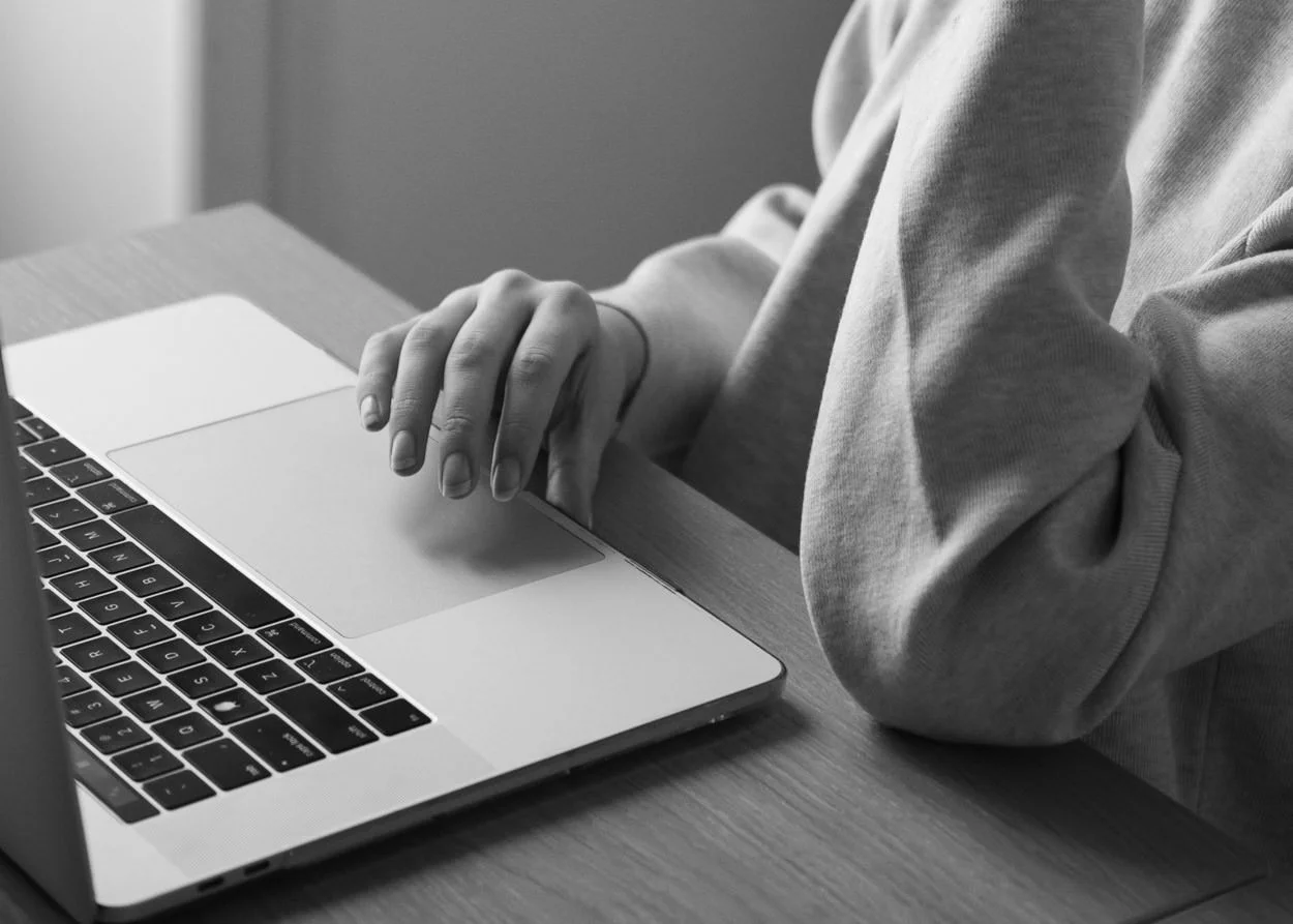 black and white close up image of a woman's hand rested on a laptop keyboard
