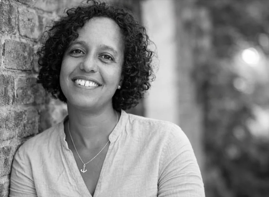 black and white photo of mixed race lady smiling leaning against a wall