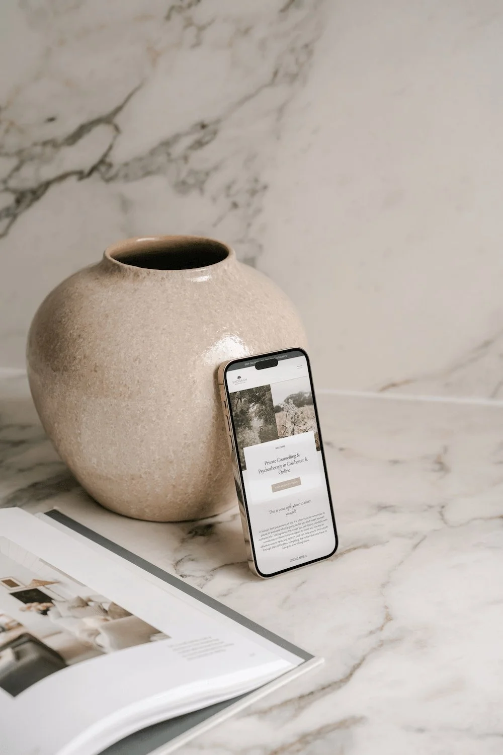mock up of a therapy website on a mobile phone resting against a cream vase