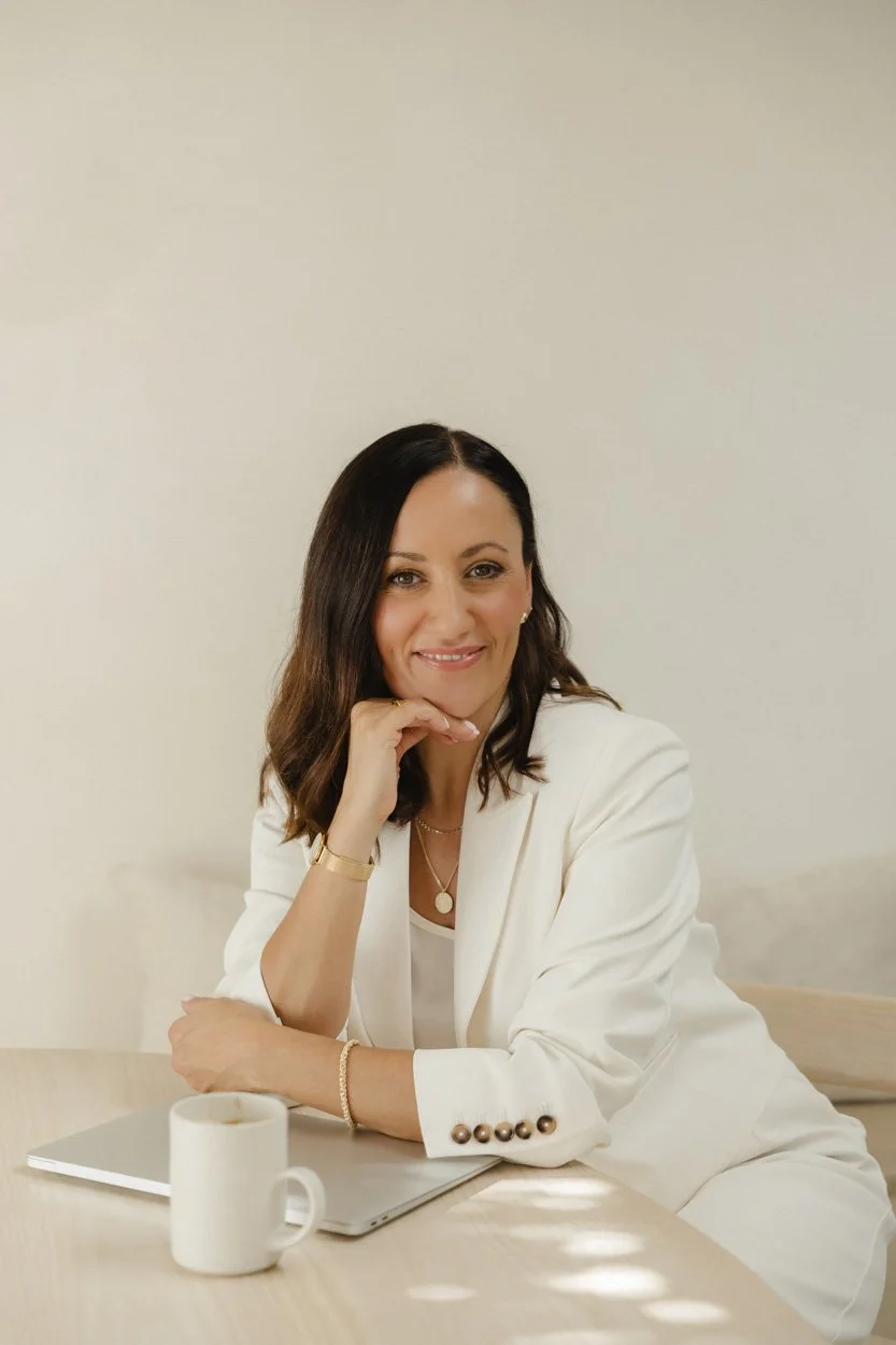 woman sitting at desk wearing a white suit with a laptop