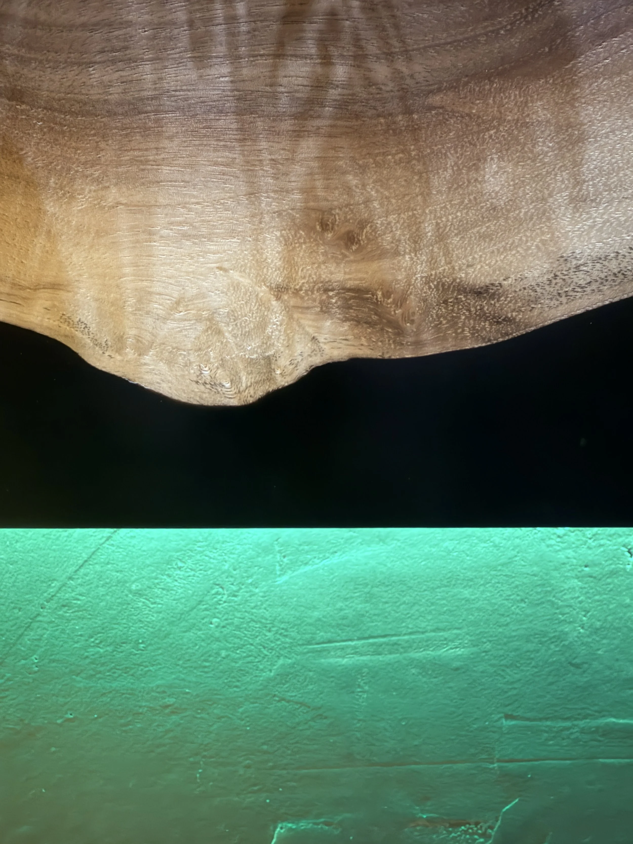 Close-up of a wooden epoxy mantle with visible grain and a micro-cement textured background beneath it, subtly illuminated by LED lights integrated into the custom mantle.
