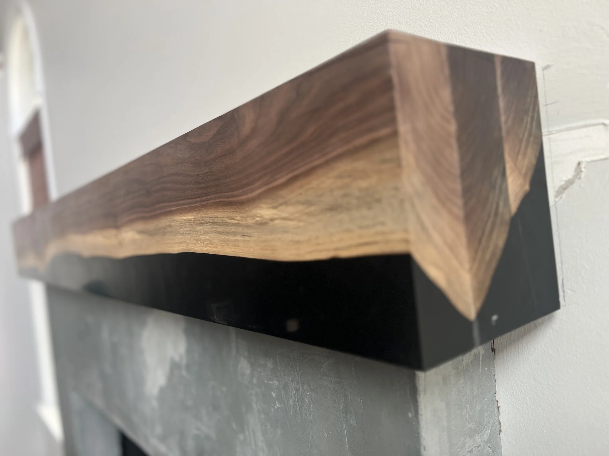Close-up of a wooden shelf with a black underside, mounted on a wall with grey and white textured paint.