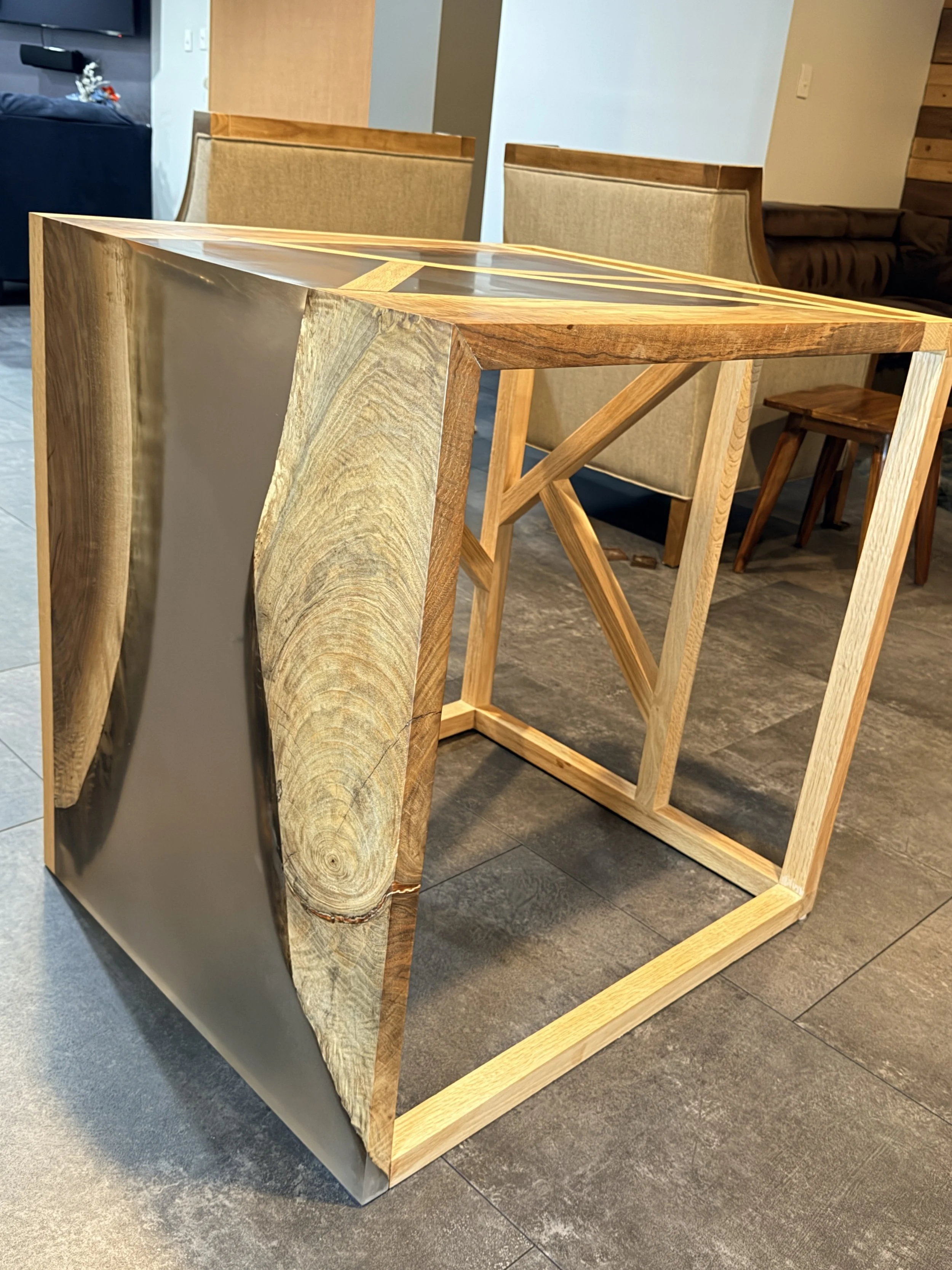 A wooden desk with a natural wood finish, featuring a live edge on one side, and a geometric wooden frame supporting the tabletop.