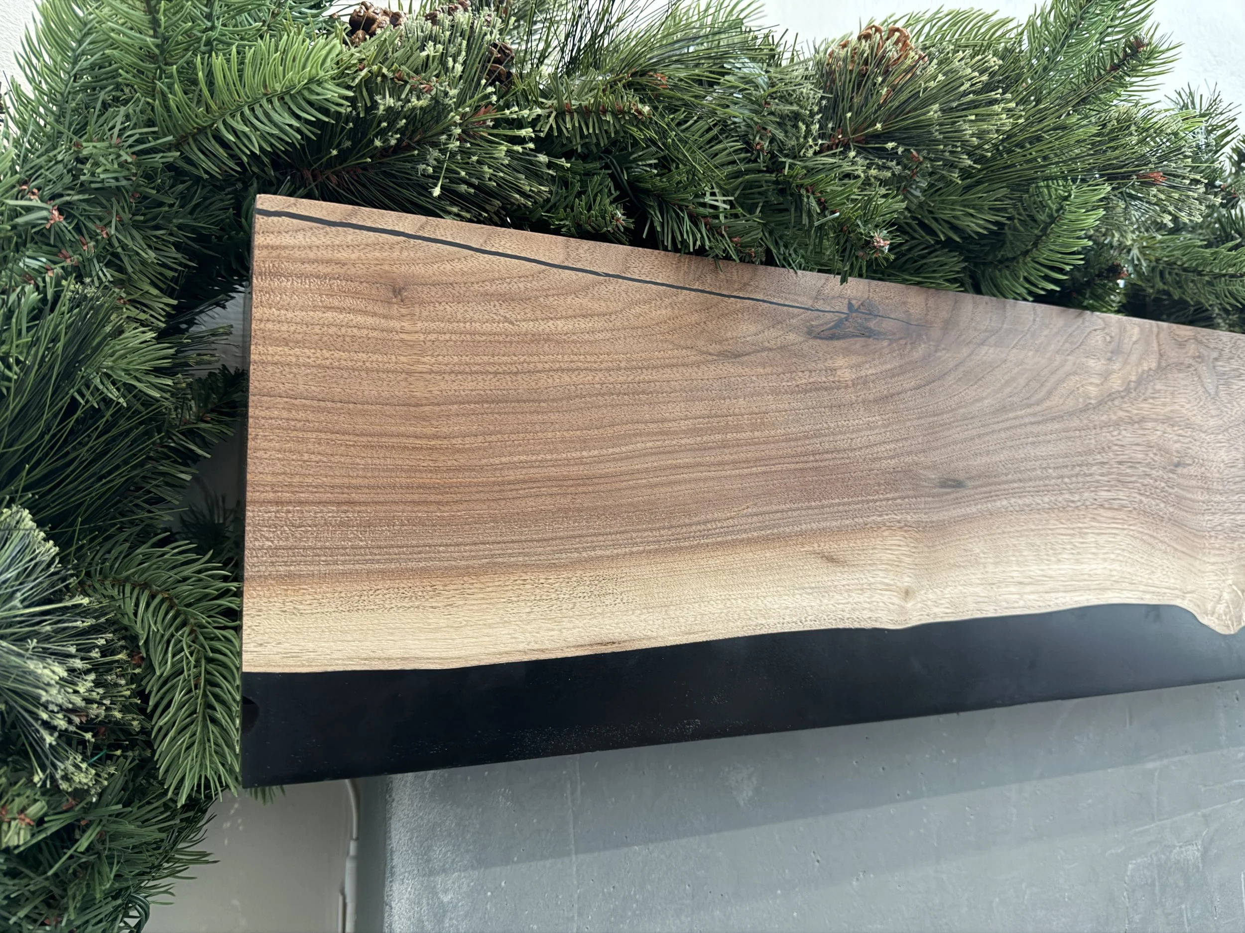 A wooden table with a black border surrounded by green pine branches.